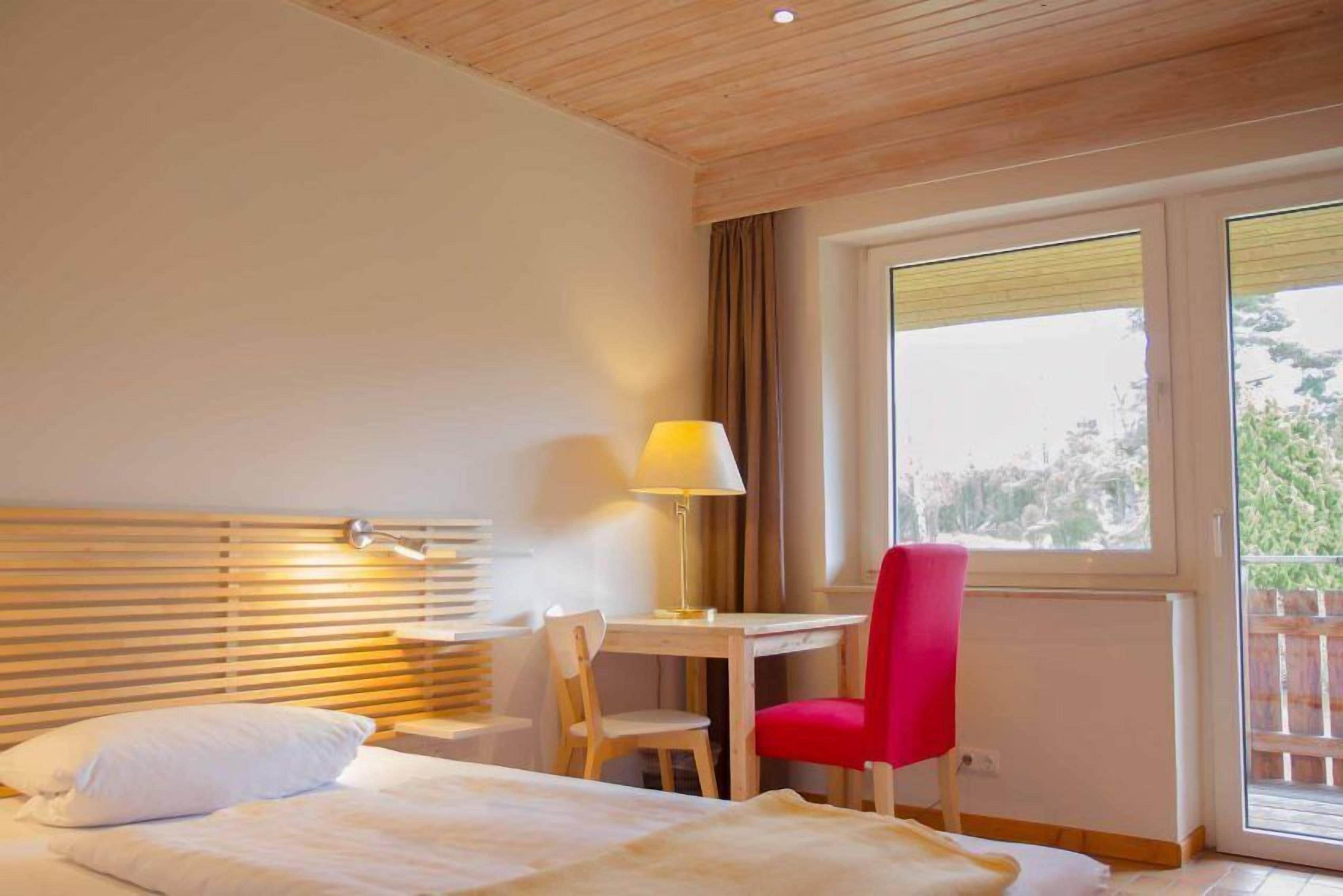 A bedroom with a bed, a desk, a chair, and a window with curtains.