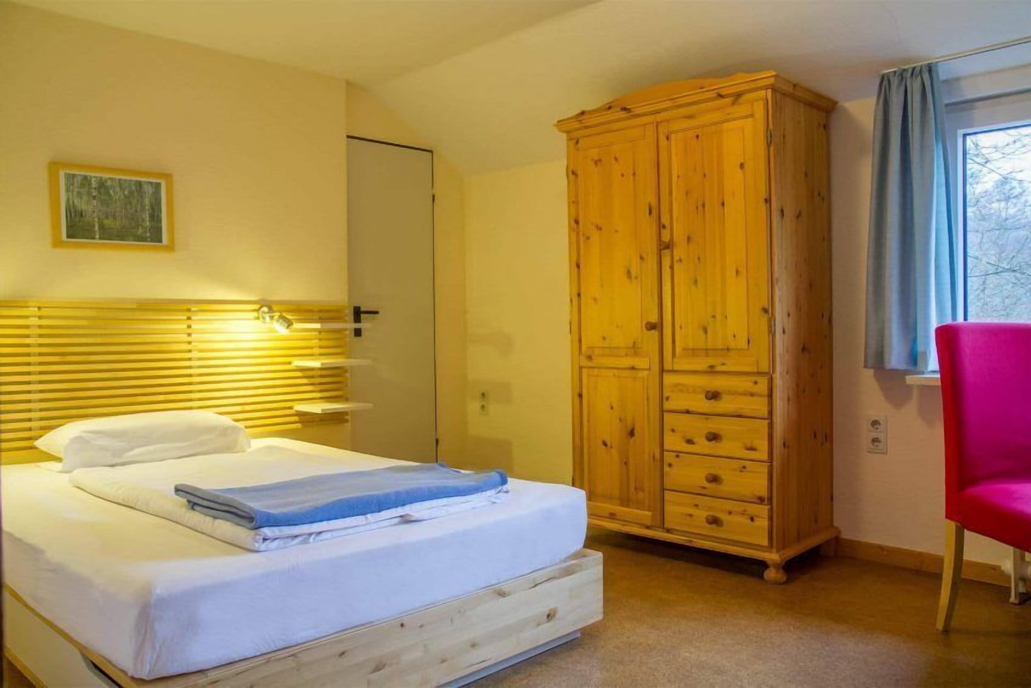 Een slaapkamer met een houten bed, een garderobe, een stoel en een raam met gordijnen.