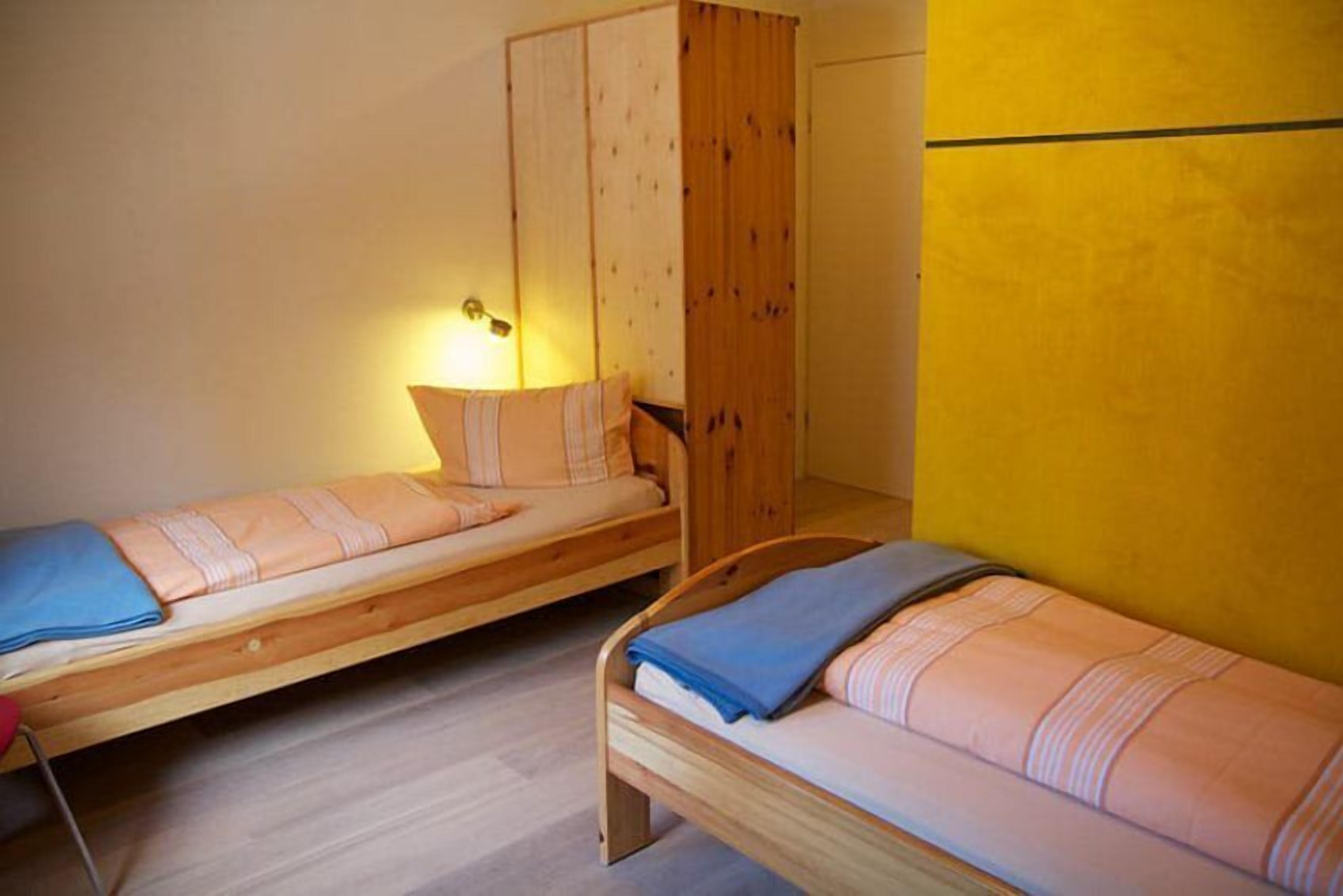 Dos camas individuales con cabeceros de madera y ropa de cama azul, un armario de madera y una pared amarilla.