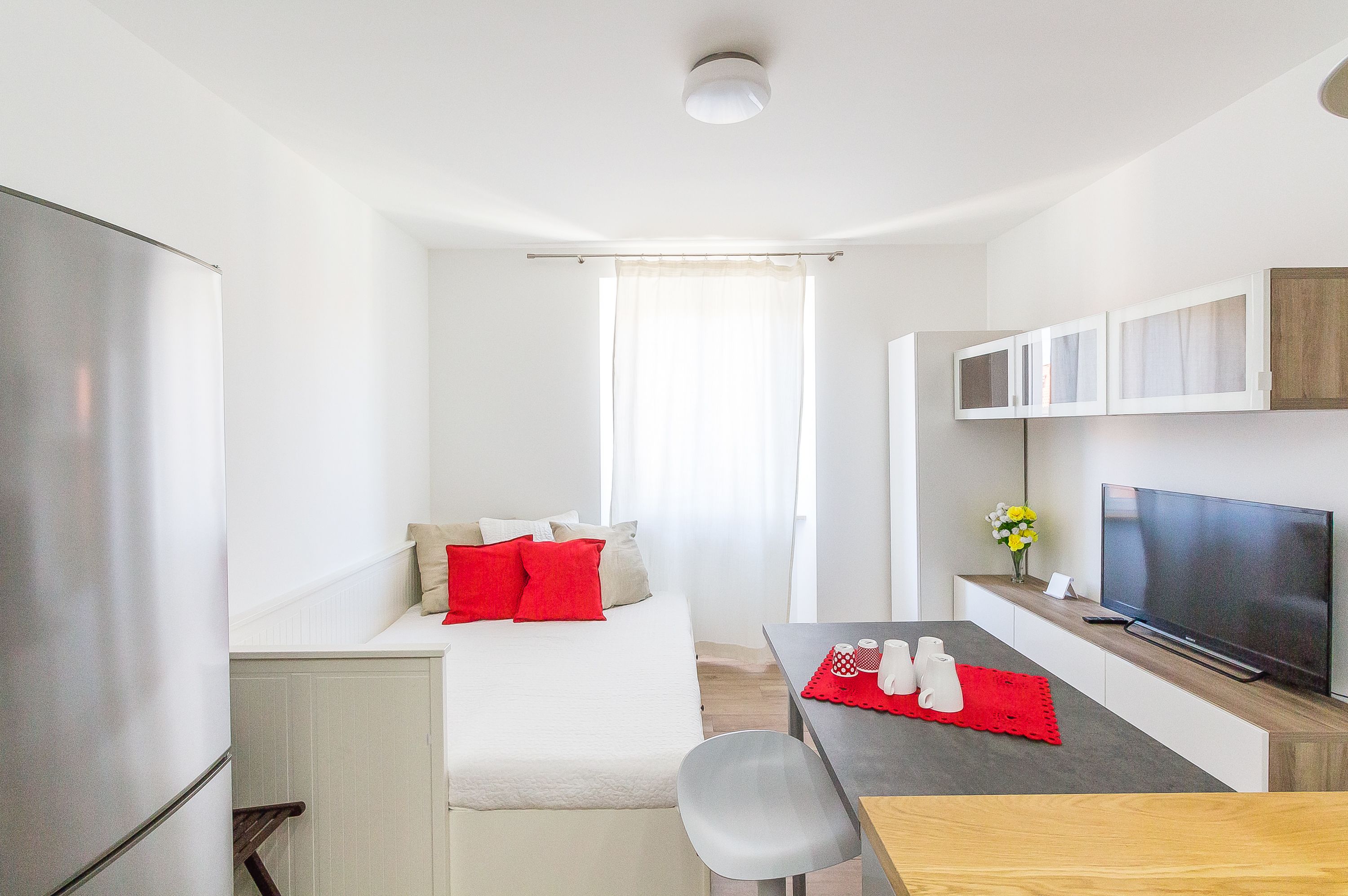 A compact room with a bed, a dining table, a TV, and a refrigerator.