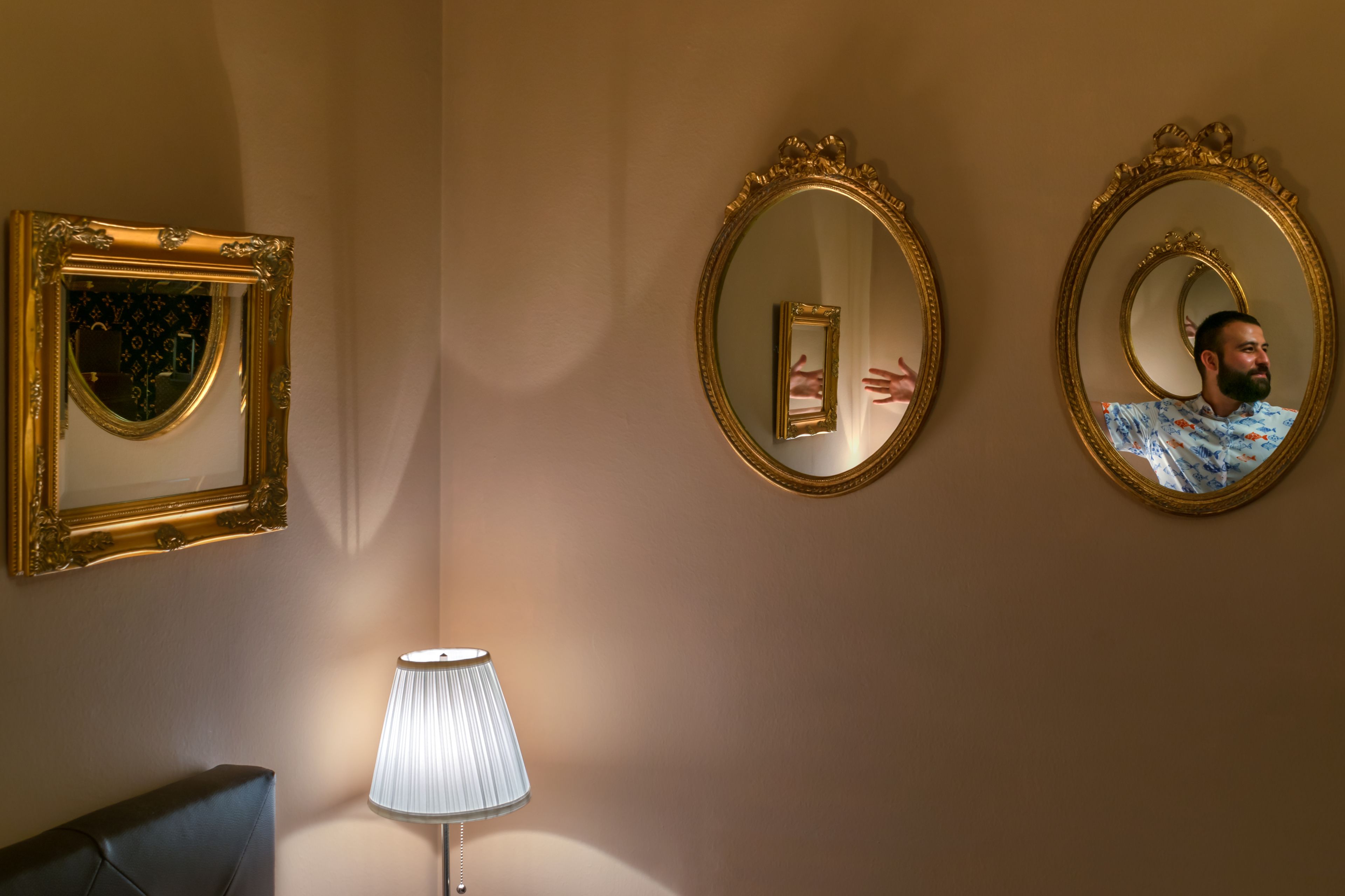 Et værelse med to dekorative, gyldne spejle på væggen, en moderne lampe og en mørk stol.