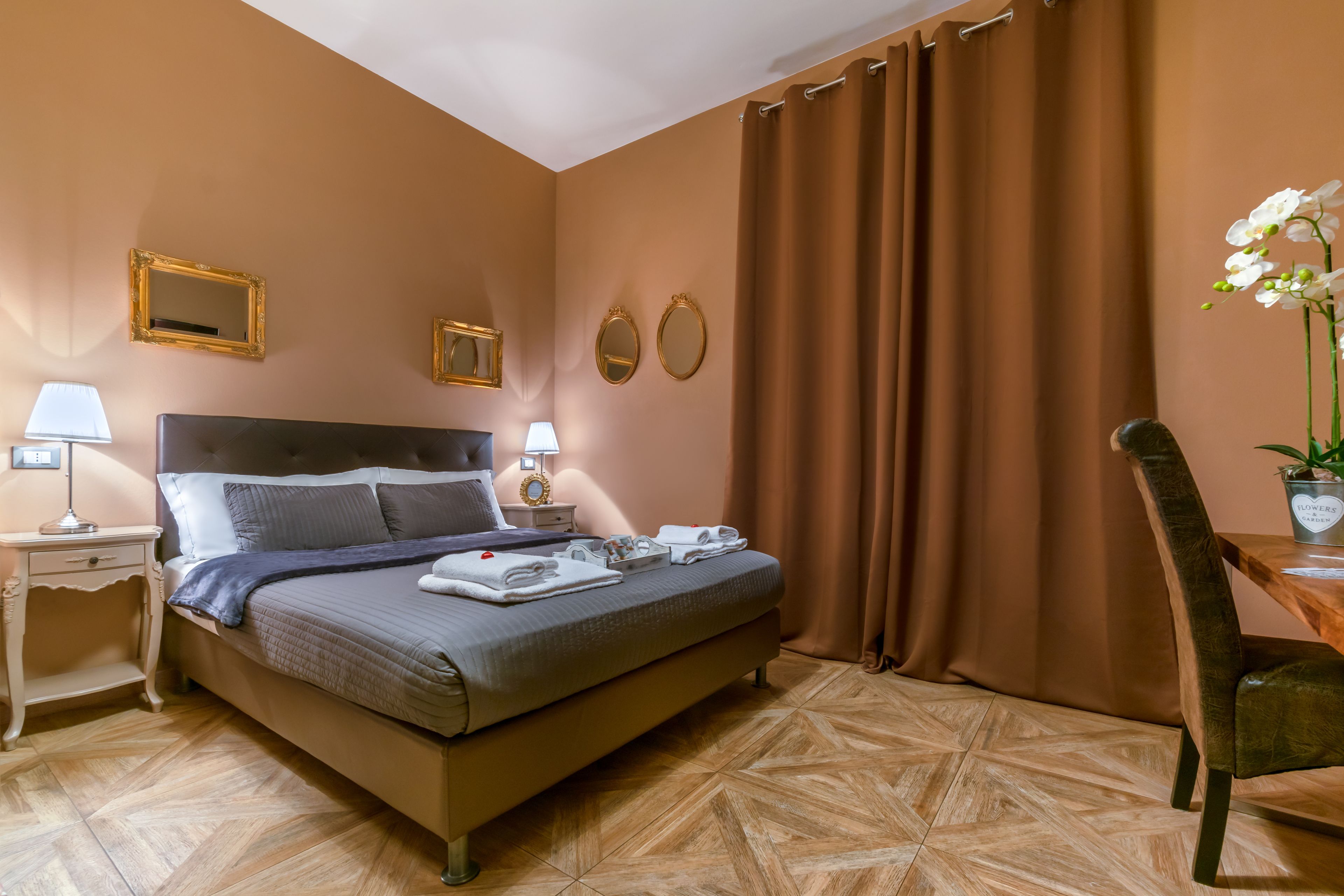 A hotel room with a large bed, two bedside tables with lamps, a chair, and a potted plant.