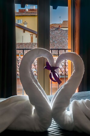 Handdoeken gevouwen in de vorm van een hart op een bed, met uitzicht op een gebouw met betegelde daken door een raam.