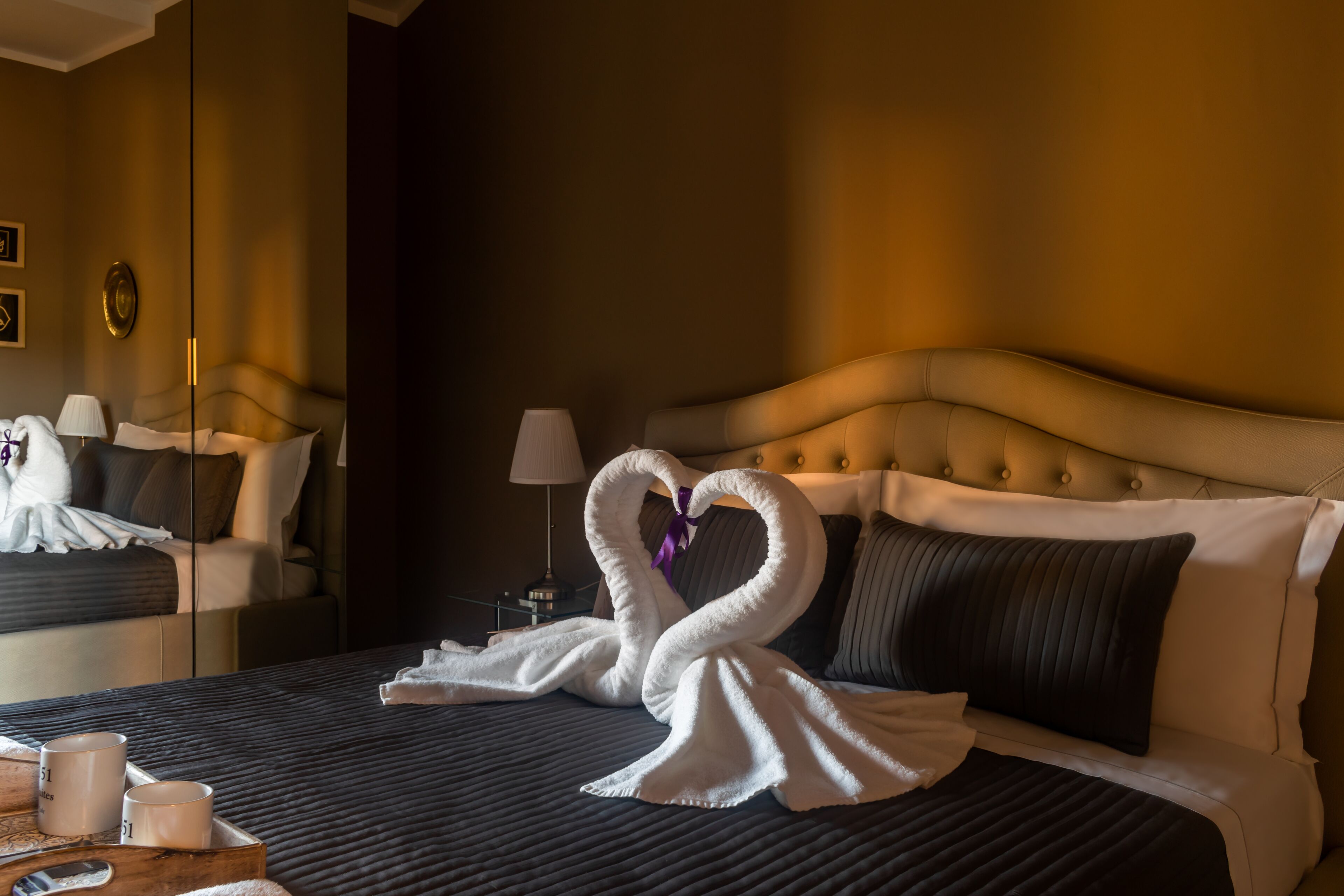A hotel room with a bed, pillows, a bedside table with a lamp, and a mirror.