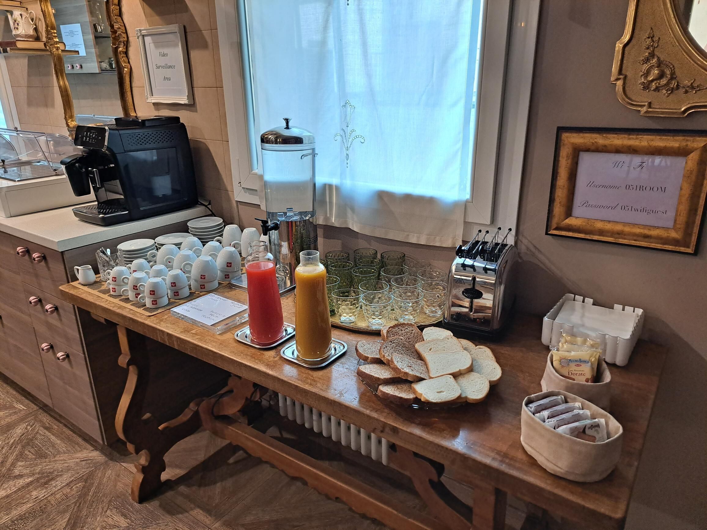 Una barra de desayuno con una máquina de café, un dispensador de agua y diversas opciones para el desayuno, como pan, jugo y cereales.