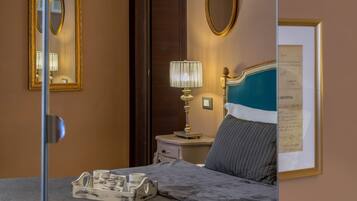 Una habitación de hotel con una cama, una mesita de noche, una lámpara, un certificado enmarcado en la pared y un espejo.