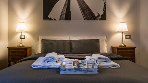 Un letto rifatto con cura, asciugamani, un vassoio con prodotti per la colazione e una cornice con un'immagine di edifici sulla parete.