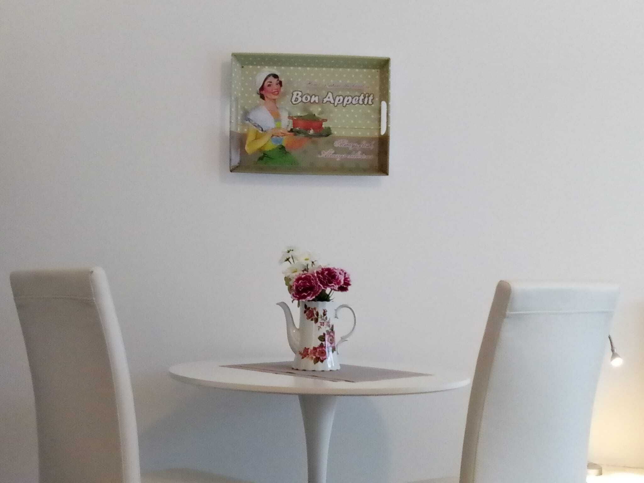 A dining area with a small round table, two chairs, and a floral vase.