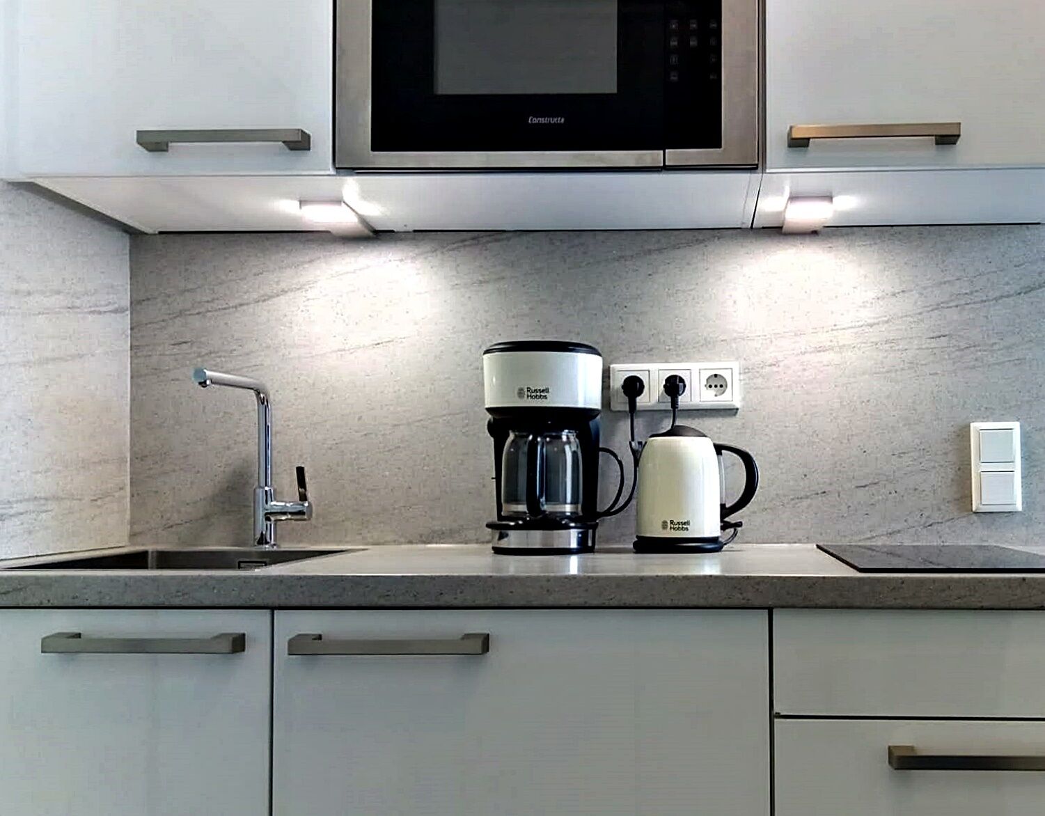 A modern kitchen with a built-in microwave, a coffee maker, and a kettle on the countertop.