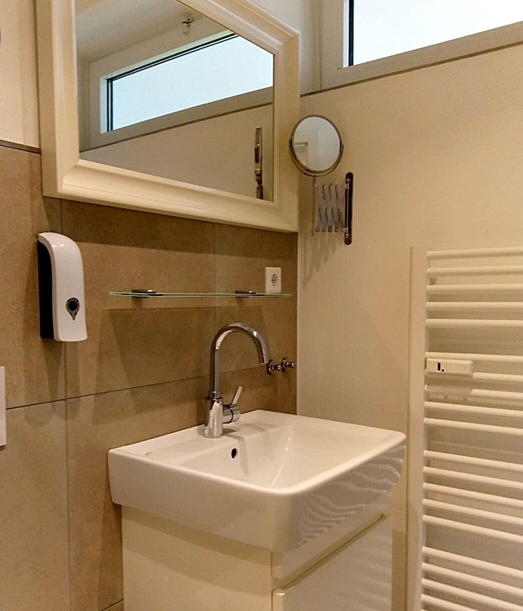 Un baño con lavamanos blanco, un espejo, un perchero para toallas y un calentador.