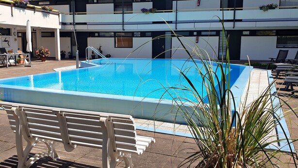 A rectangular swimming pool with a clear blue water surface, surrounded by a tiled deck. There are lounge chairs and a bench along the poolside. - Apartment Regina am schönen Möhnesee (Moehnesee)