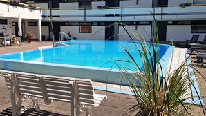 A rectangular swimming pool with a clear blue water surface, surrounded by a tiled deck. There are lounge chairs and a bench along the poolside. - Apartment Regina am schönen Möhnesee (Moehnesee)