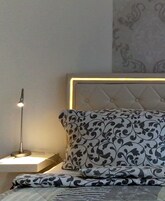 Cama bem arrumada com roupa de cama estampada, abajur e cabeceira decorativa.