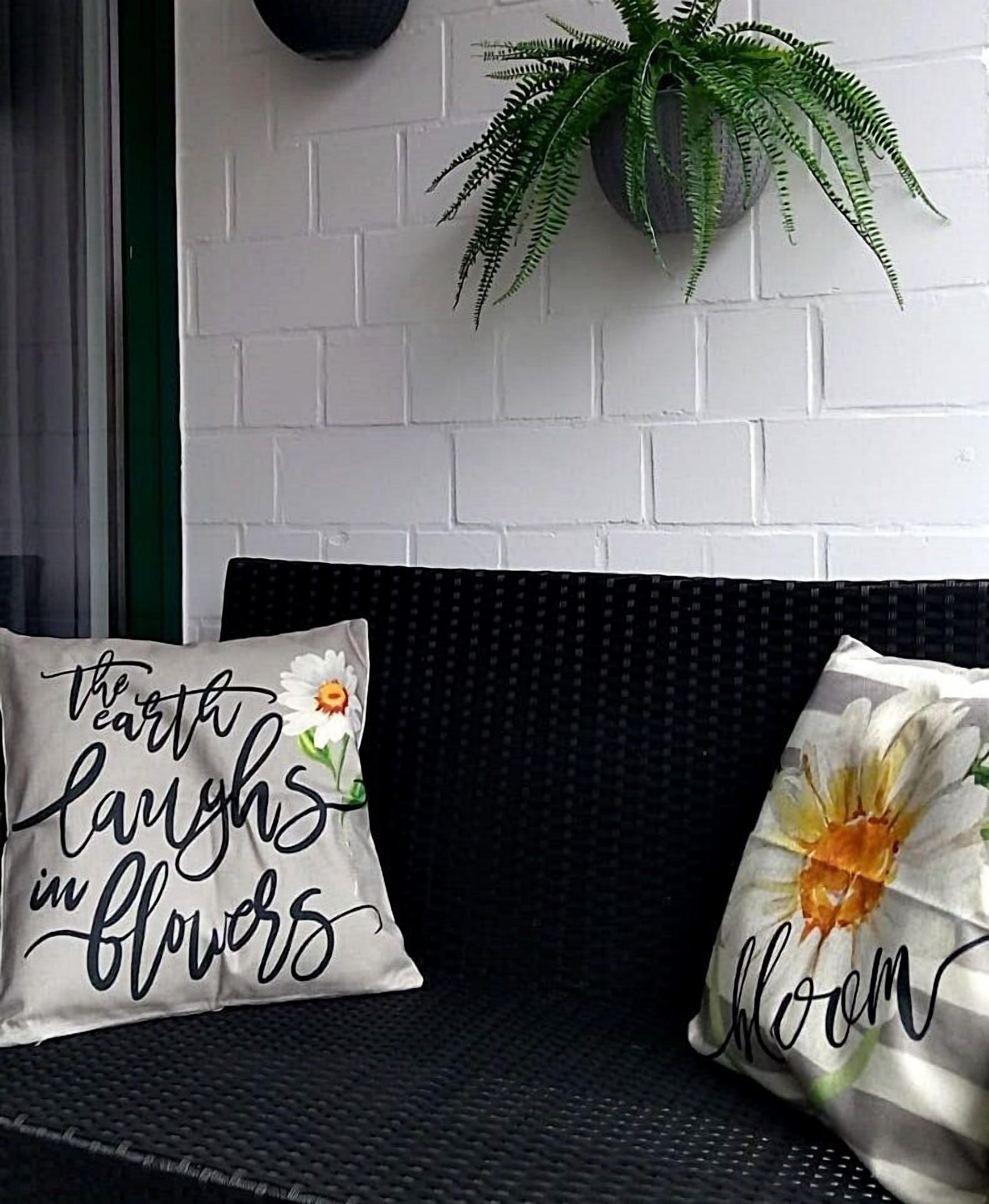 Ein schwarzes Rattan-Sofa mit zwei Zierkissen, eines mit einem Gänseblümchen- und das andere mit einem Sonnenblumenmuster.