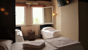 A bedroom with two beds, a bedside table, a nightstand, a wall-mounted TV, and a window with curtains. - Durak Hotel (Bodrum)