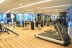 A modern gym with various exercise equipment, including treadmills and weight machines, and a carpeted floor.