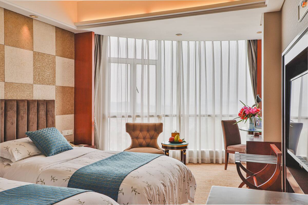 Ein Hotelzimmer mit einem großen Bett, einem Sessel, einem kleinen Tisch mit Blumenvase und einem Fernseher.