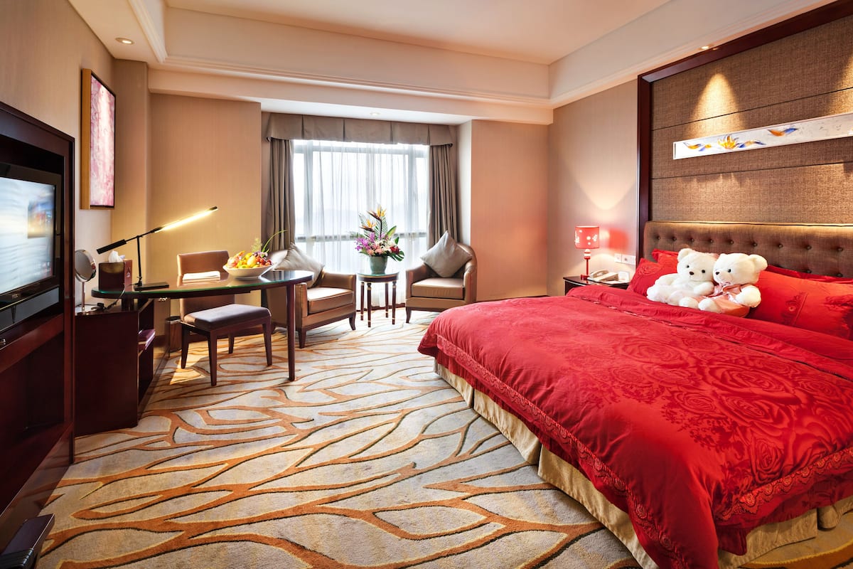 Ein Hotelzimmer mit einem großen Bett, einem Schreibtisch, einem Sessel, einem Fernseher und einem Fenster mit Vorhängen.