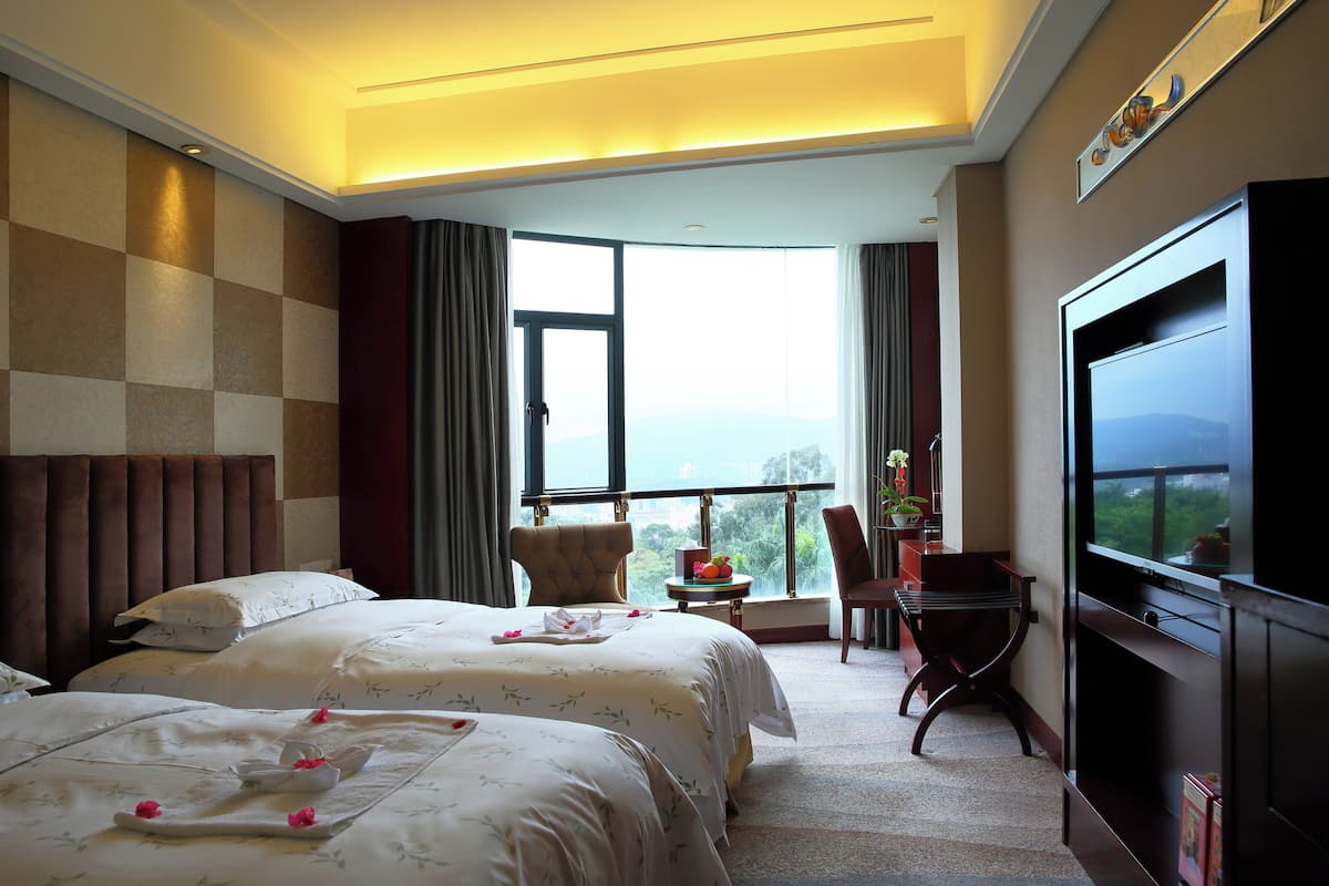 Ein Hotelzimmer mit zwei Betten, einem Fernseher, einem Schreibtisch und Blick ins Freie.