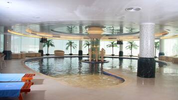 Una piscina interior amplia con zonas de descanso y palmeras.