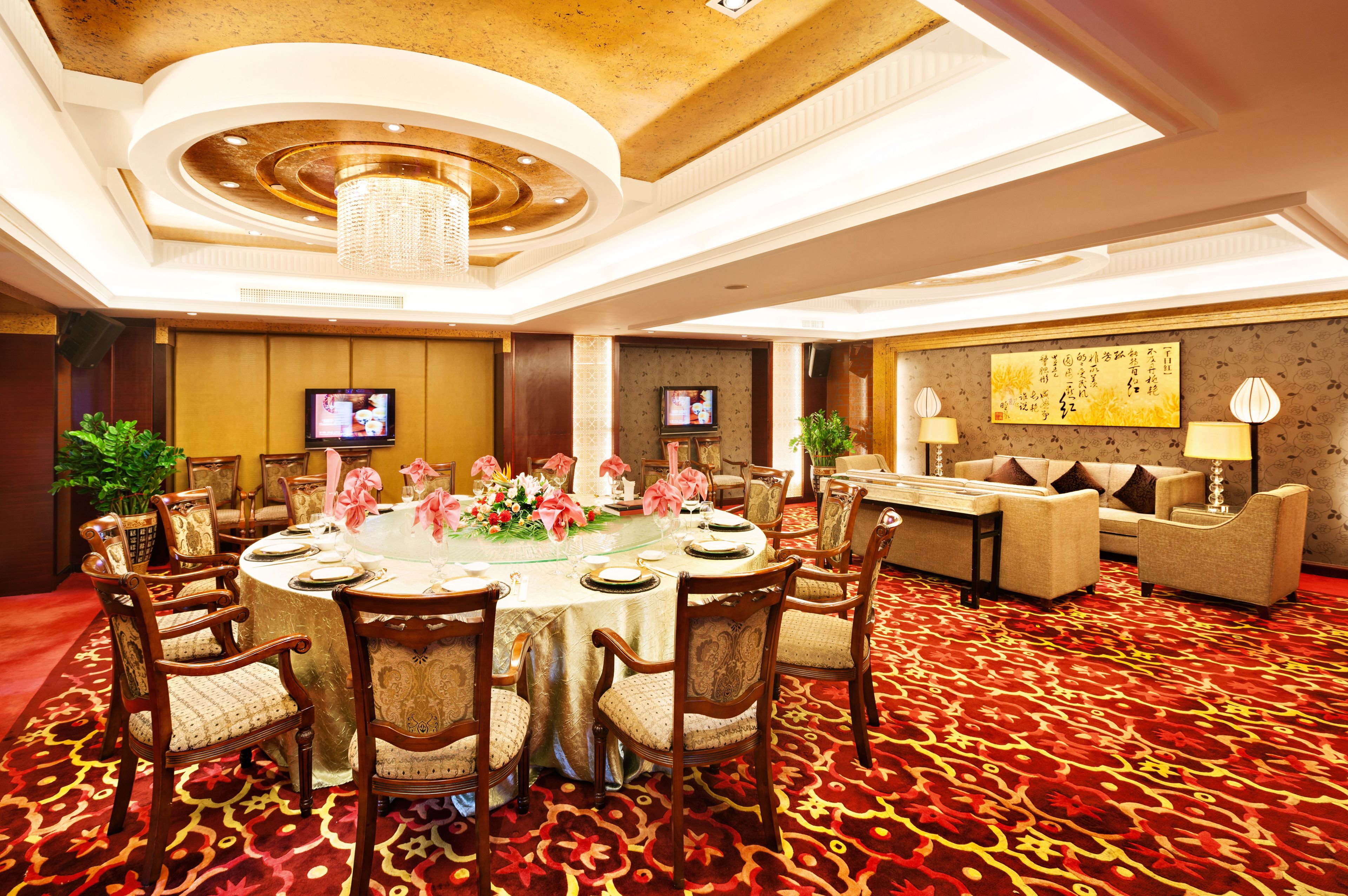 A hotel room with a round dining table set for six, surrounded by wooden chairs. There is a sofa and a television mounted on the wall.