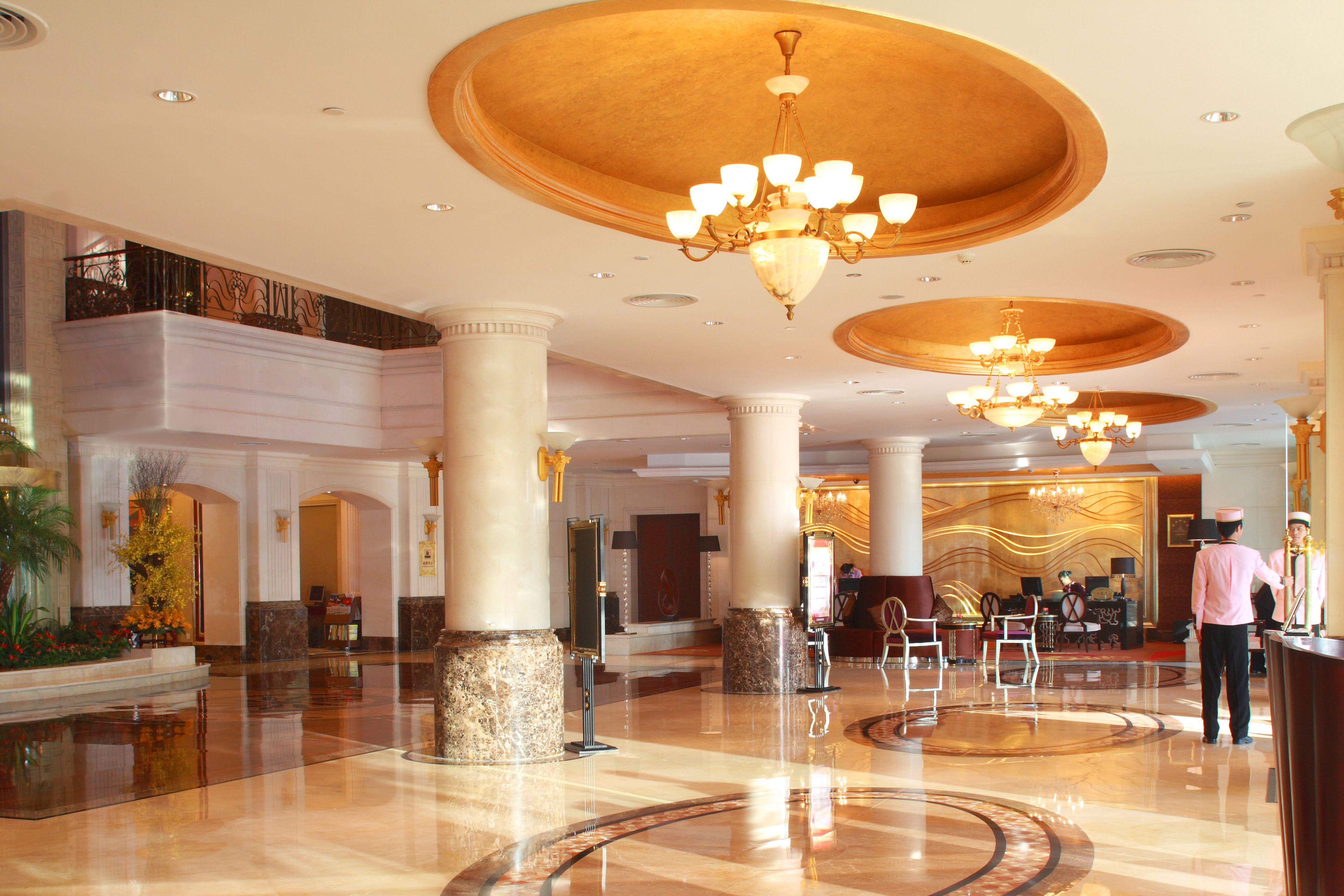 A spacious lobby with marble flooring, large columns, and ornate chandeliers.