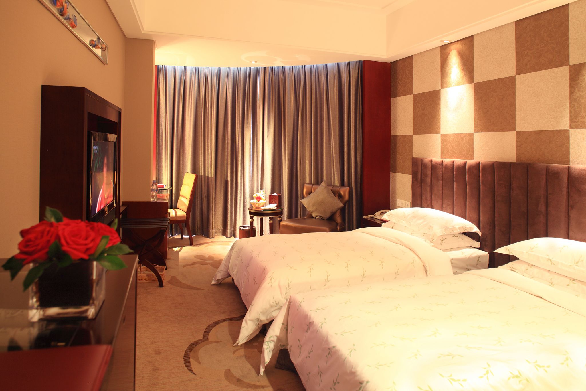 A hotel room with two beds, a desk with a computer, a chair, a TV, and a window with curtains.