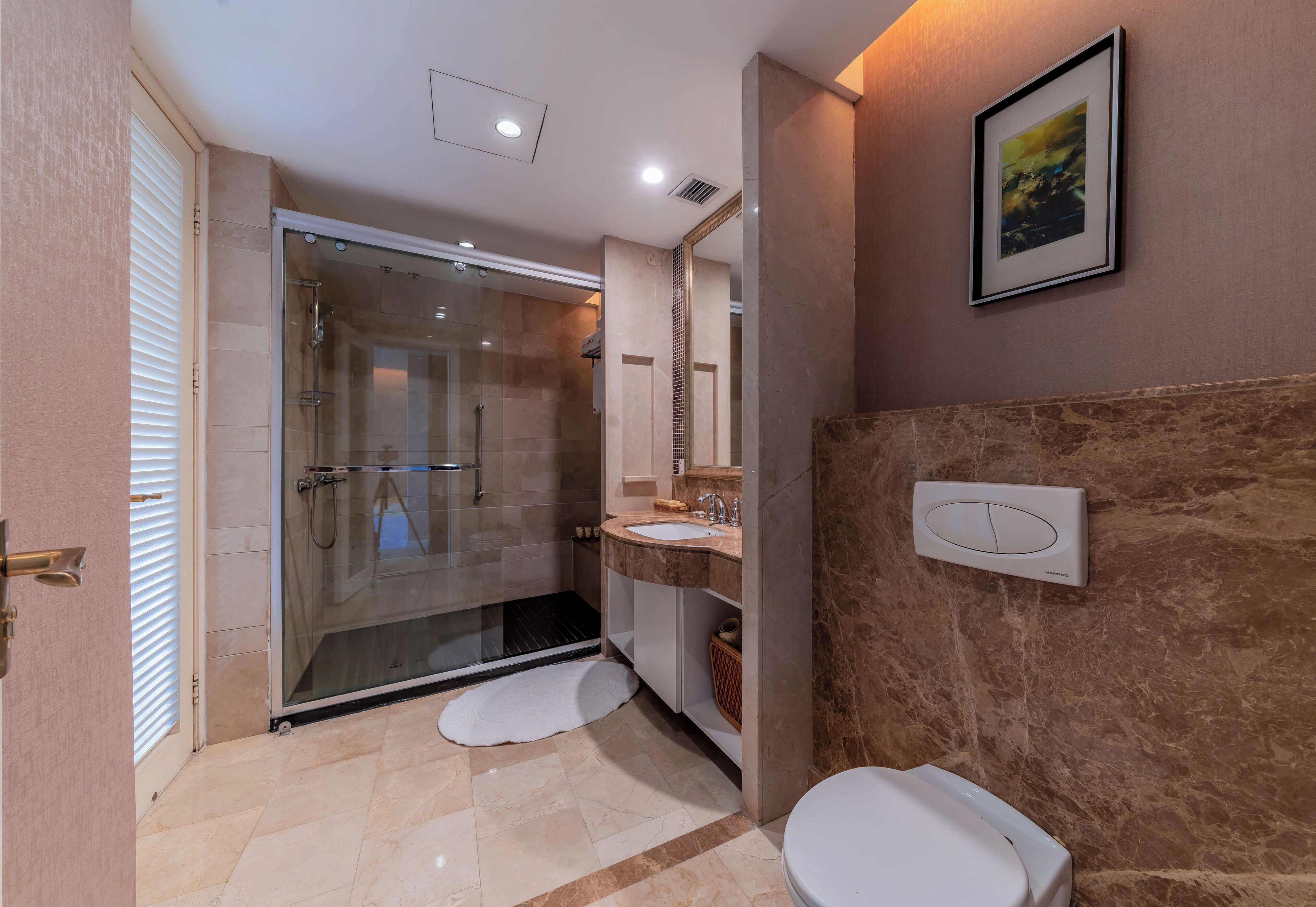 Un baño moderno con ducha envuelta en vidrio, un lavamanos blanco y una pared de mármol.