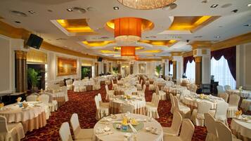 A banquet hall with round tables, white chairs, and a red carpet.