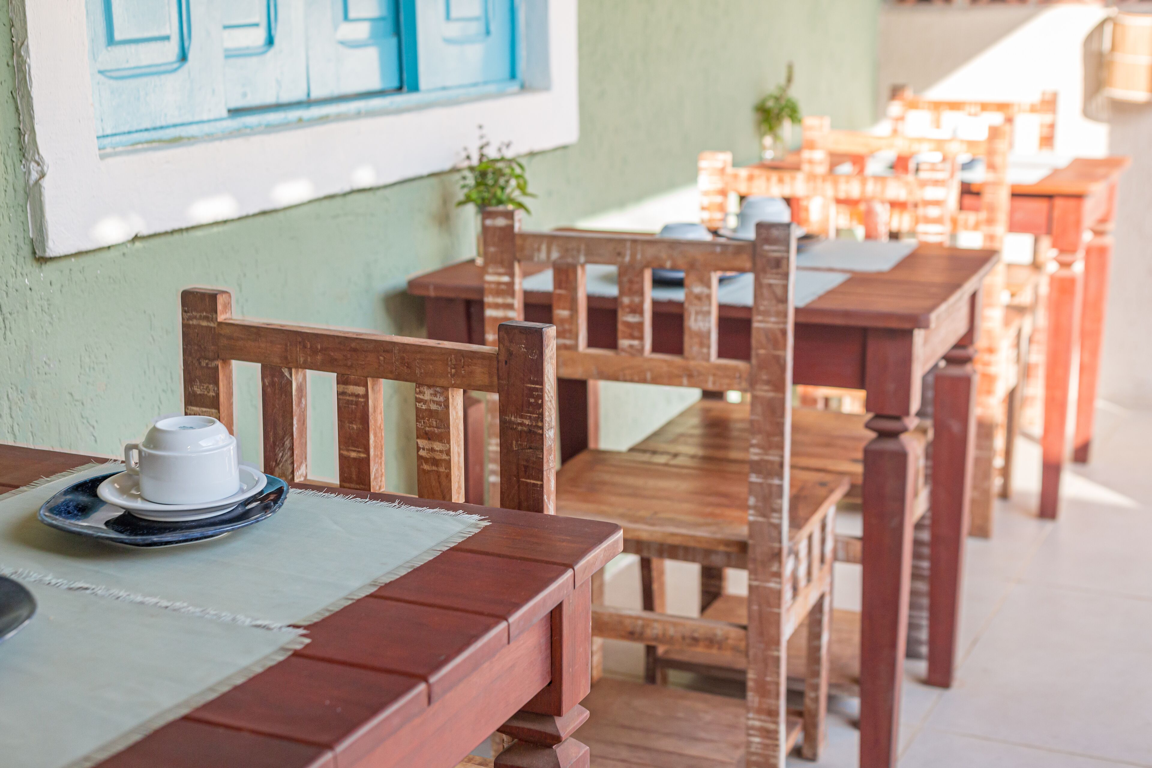 A wooden dining table with a white cup and saucer, a blue plate, and a white placemat.