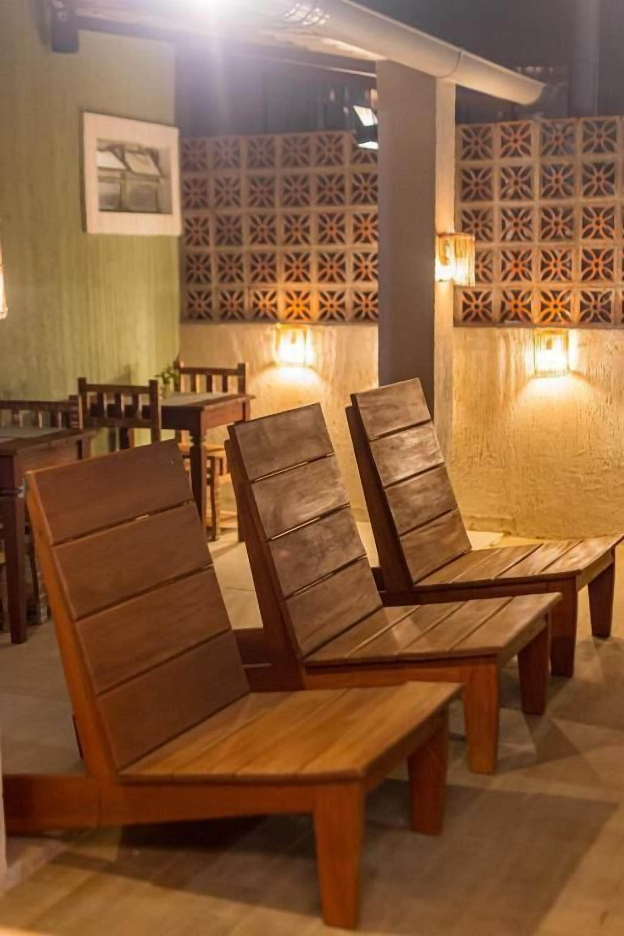 A seating area with wooden benches and tables, a patterned wall, and wall-mounted lights.