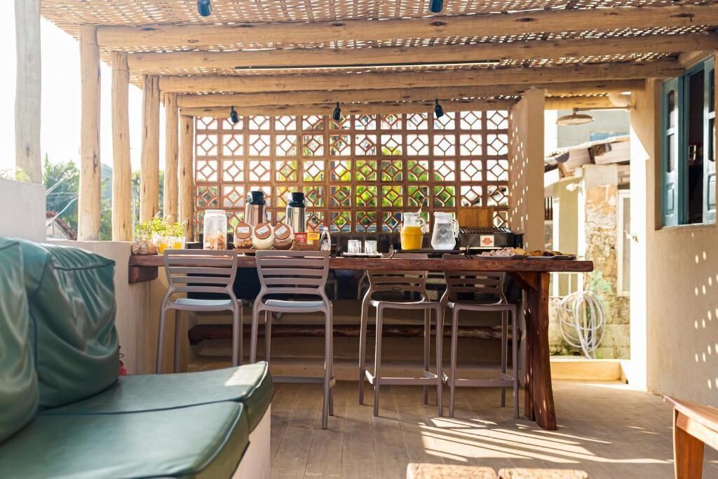 Un espacio comedor al aire libre cubierto con una mesa de madera, sillas de metal y diversos objetos sobre la mesa, incluyendo una cafetera, una jarra de vidrio y una botella.