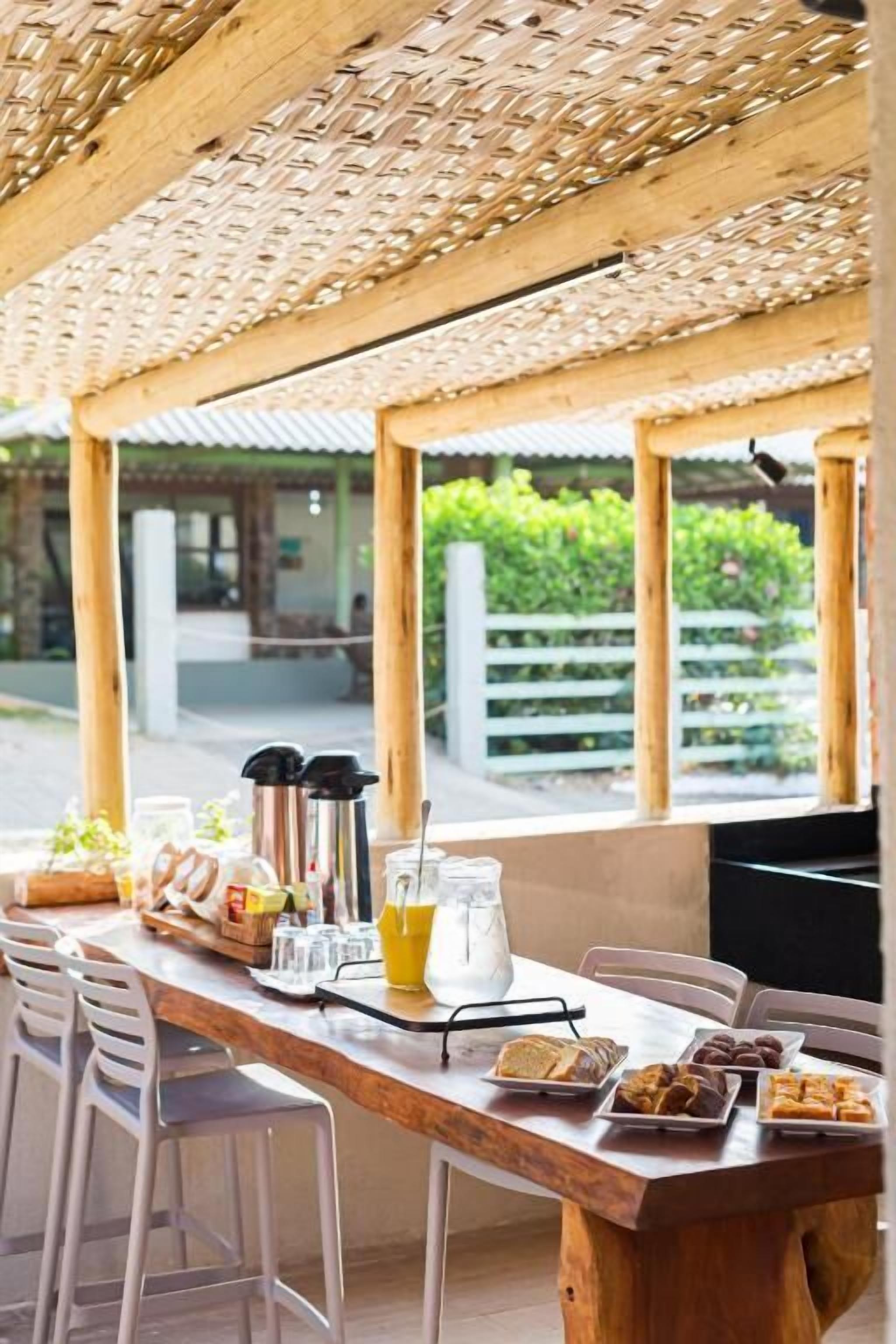 An outdoor dining area with a wooden table set for breakfast, including bread, pastries, and a coffee pot.