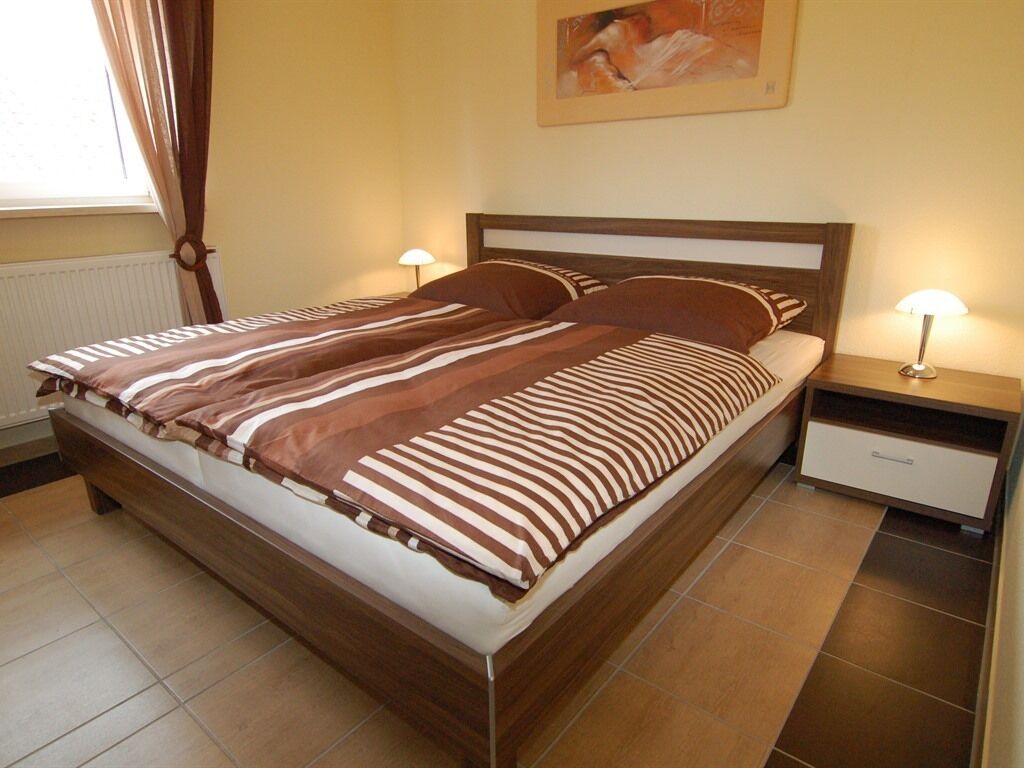A double bed with striped bedding, a nightstand with a lamp, and a radiator on the wall.