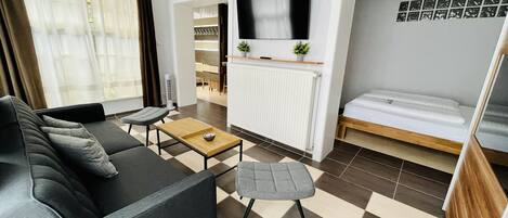 Una sala moderna con sofá, una mesita, un televisor y una cama.