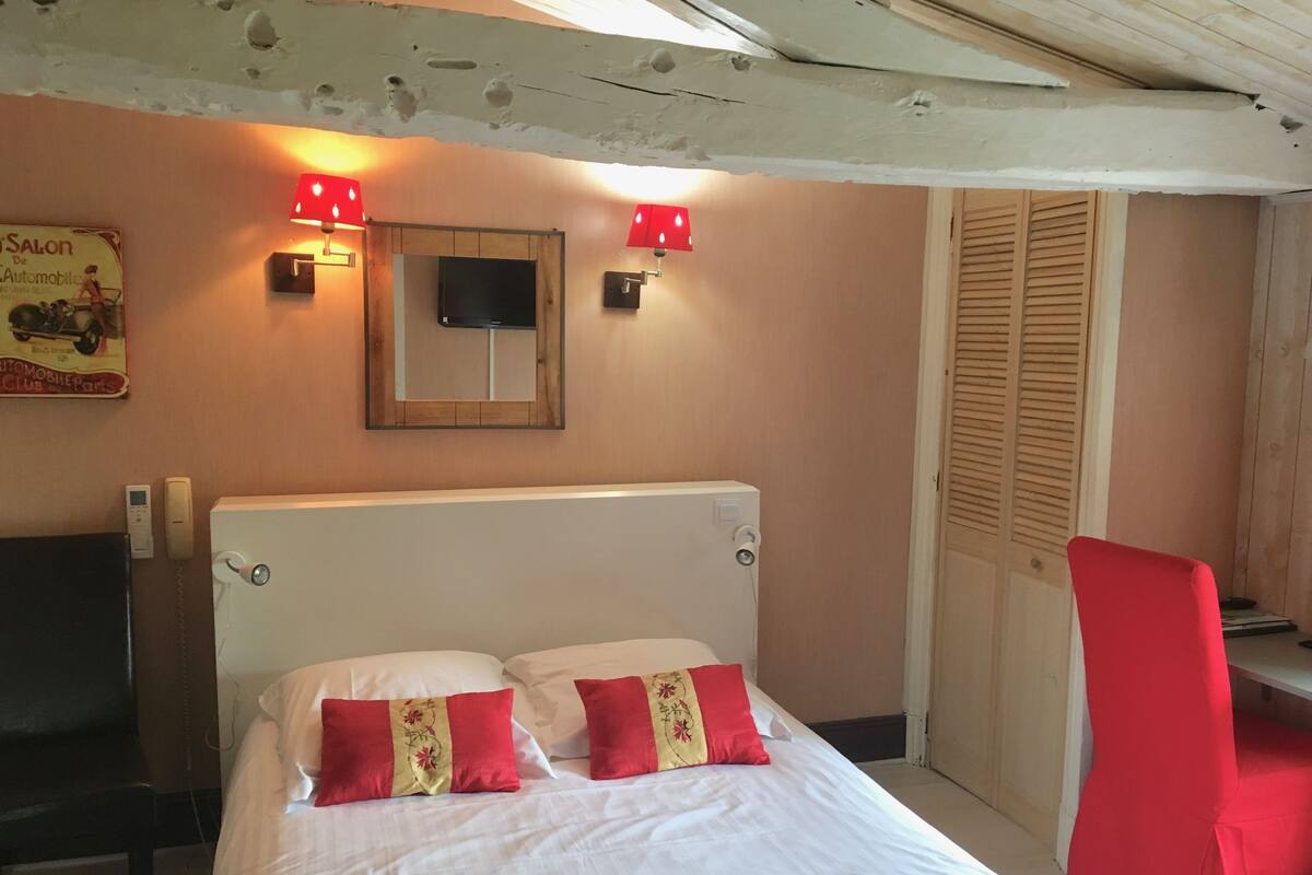 Un dormitorio con una cama, una silla roja, una puerta de madera y luces fijadas a la pared.