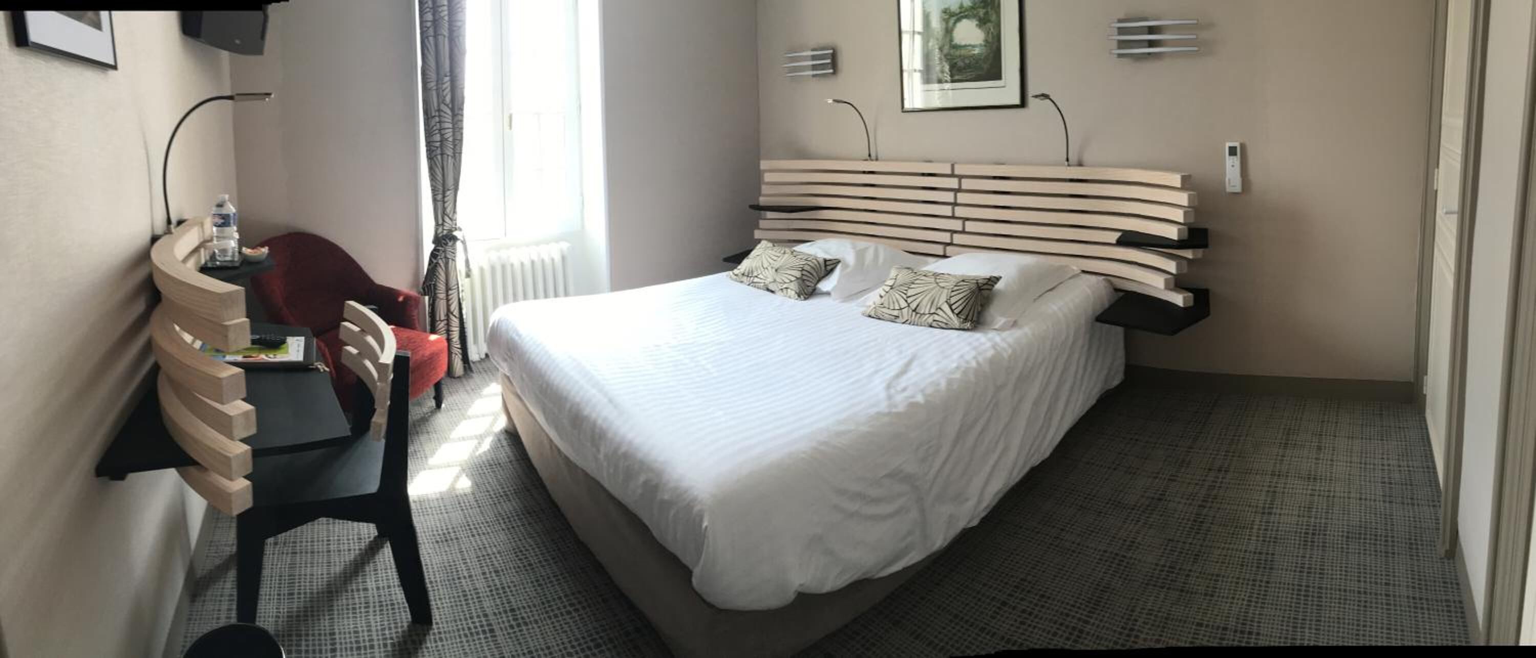 Een hotelkamer met een bed, bureau, stoel en een raam met gordijnen.