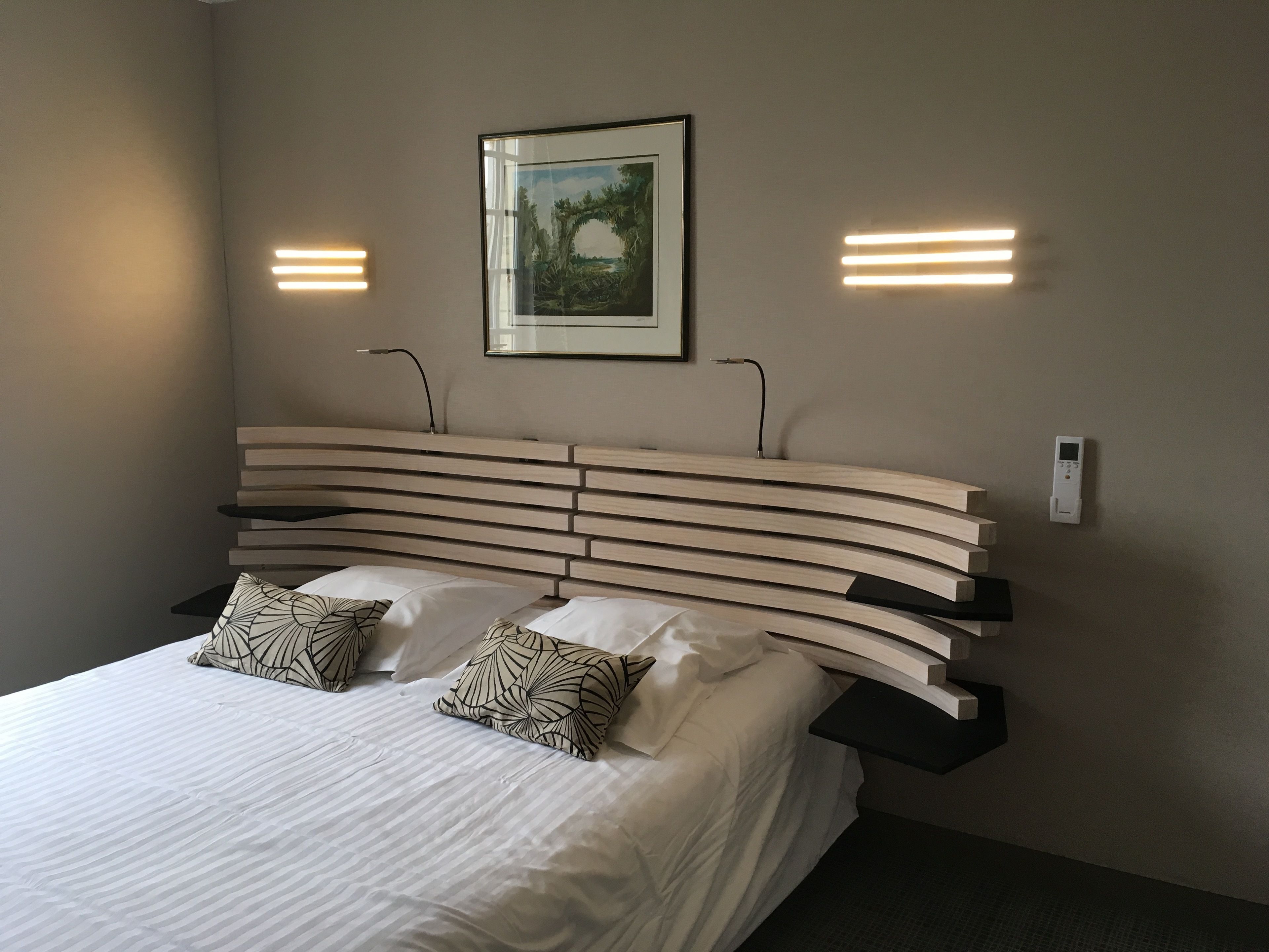 Una habitación de hotel moderna con una cabecera curvada, dos mesitas de noche y un cuadro enmarcado en la pared.