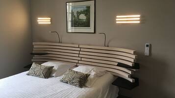 Una habitación de hotel moderna con una cabecera curvada, dos mesitas de noche y un cuadro enmarcado en la pared.