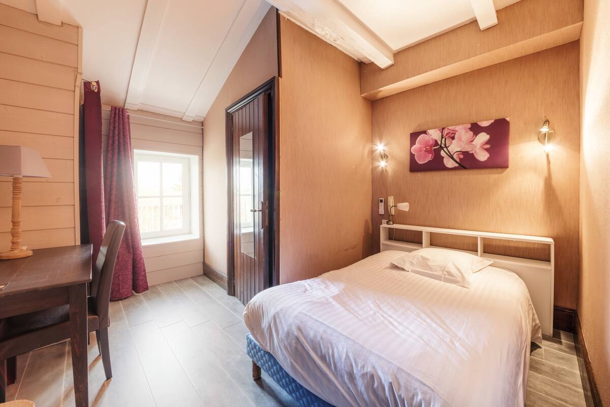 Una habitación de hotel con cama, escritorio y ventana con cortinas.