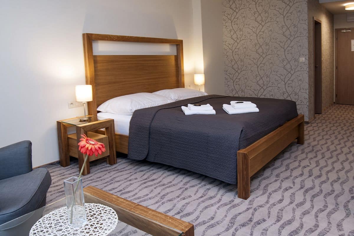 A hotel room with a wooden bed, two bedside lamps, a small table with a vase, and a patterned carpet.