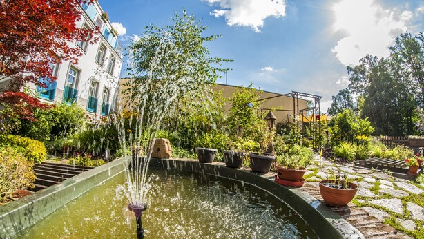 A fountain in a garden with potted plants and a building in the background. - Hotel U Zvonu (Vrchlabi)