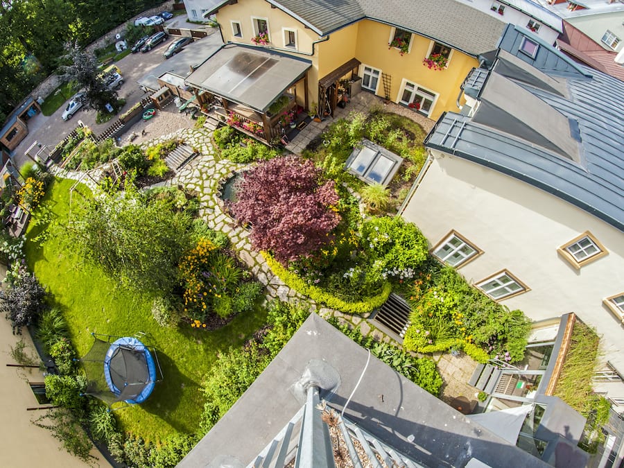 An aerial view of a residential area with a well-maintained garden, a trampoline, and a house with a sloped roof.