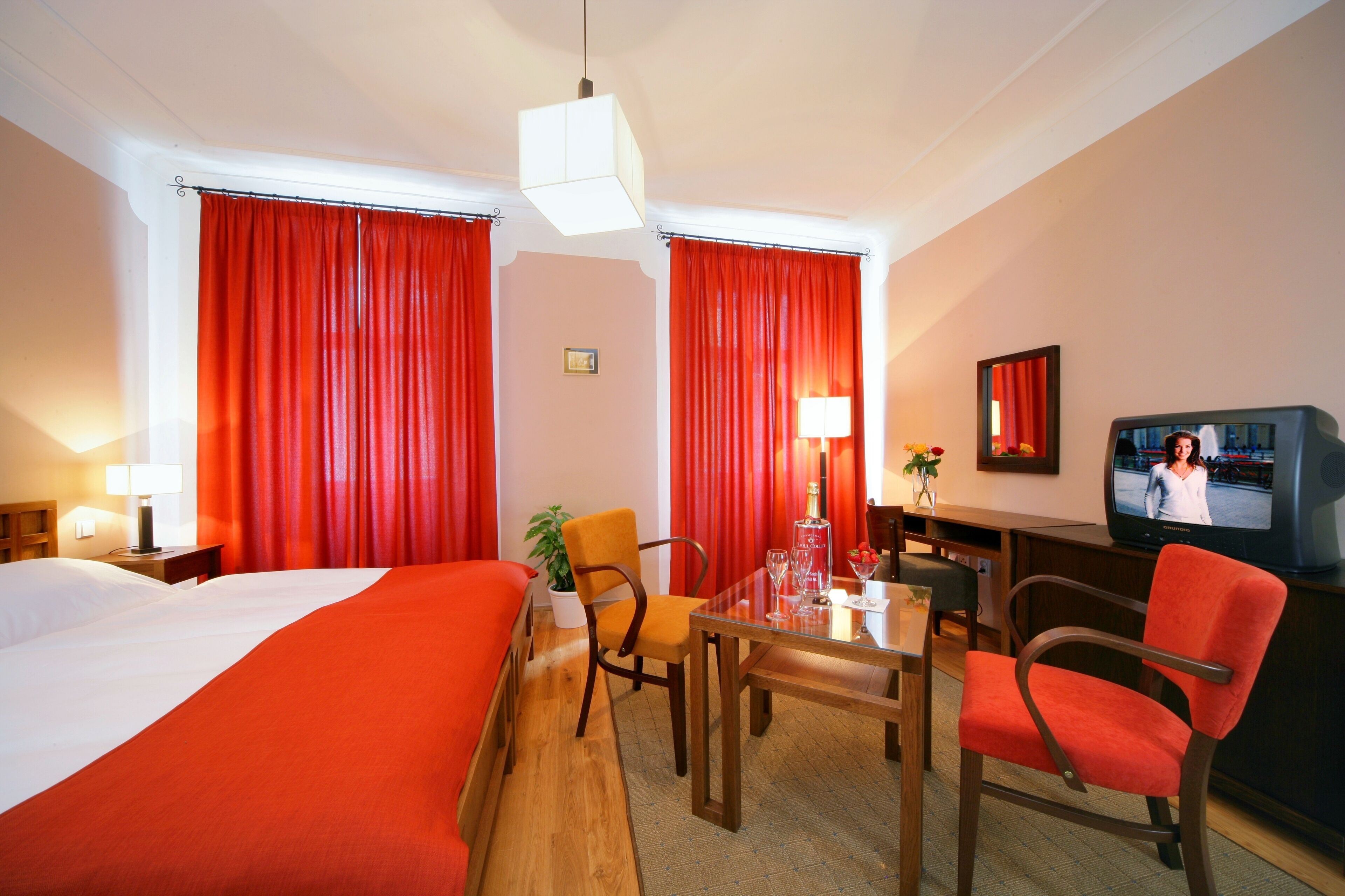 A hotel room with a bed, a desk with a chair, a television, and red curtains.