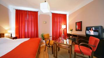 A hotel room with a bed, a desk with a chair, a television, and red curtains.