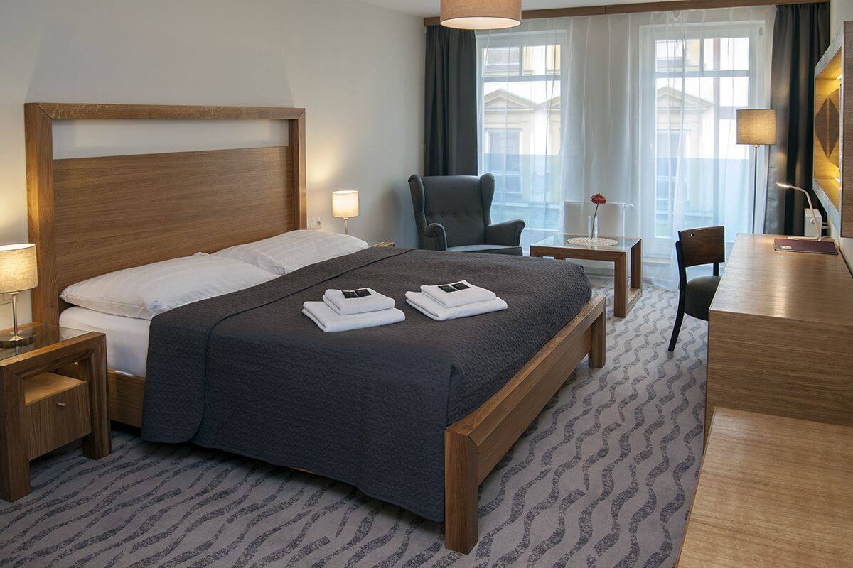 A hotel room with a large bed, a desk, a chair, and a nightstand.