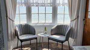 A room with two grey upholstered chairs facing a window with a view of the sea. A small table with a wine bottle and glass is between the chairs. - Lichfield House (Weymouth)