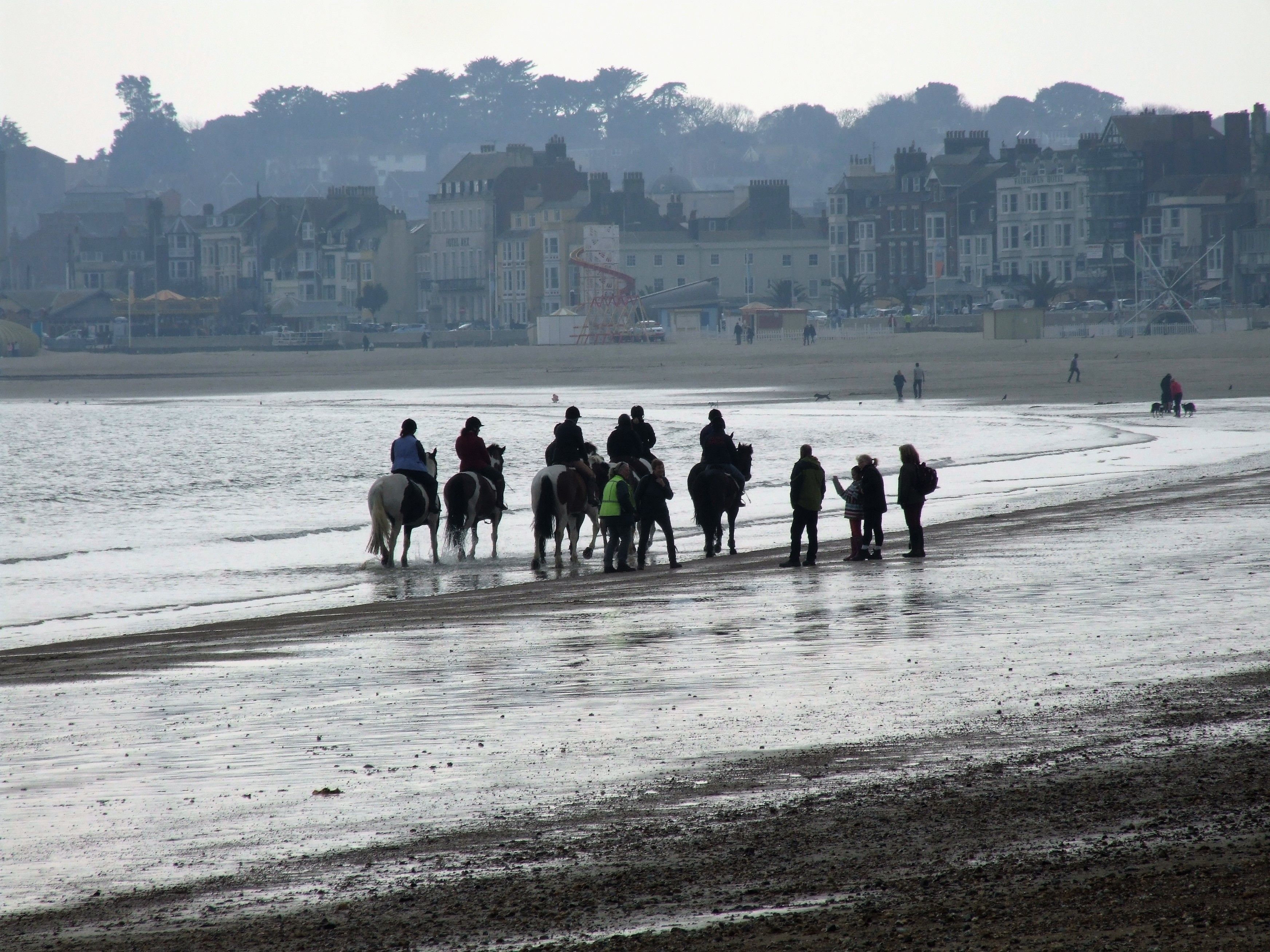 A beach with people riding horses and walking along the shore.