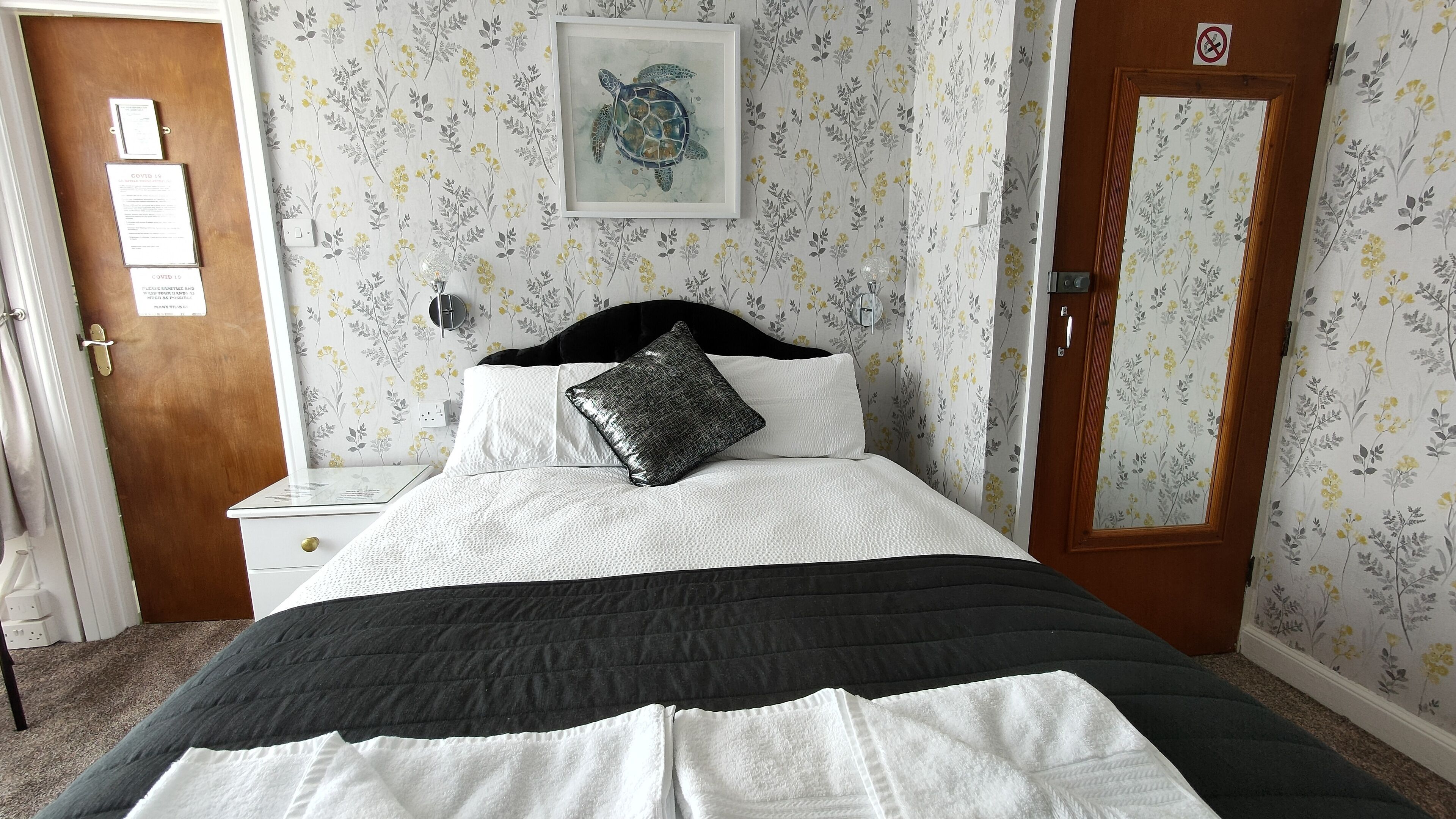 A neatly arranged bedroom with a bed, a nightstand, a framed artwork, and a door with a 'No Entry' sign.