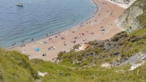 A beach with cliffs, a sailboat, and people relaxing. - Lichfield House (Weymouth)